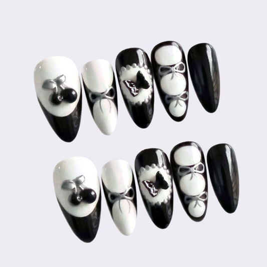 Medium almond press-on nails in black and white with 3D cherries, butterfly, and glossy details. Handmade Gothic Lolita nail art, ideal for cosplay, parties, or gifting.